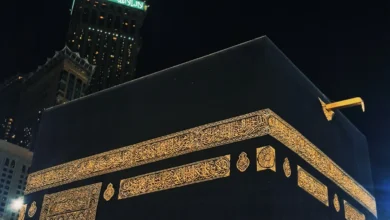 A diverse group of Muslim pilgrims in white Ihram clothing perform Tawaf, circumambulating the Kaaba in Mecca. The scene captures the devotion and unity of pilgrims during their spiritual journey, with the Kaaba's black cloth and gold-embroidered calligraphy prominently visible in the background, conveying a sense of reverence and solemnity