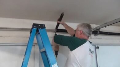 A man repairs a garage door using a ladder, demonstrating skill and focus in a home maintenance task.