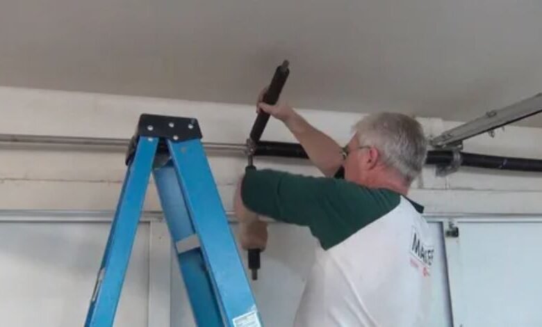 A man repairs a garage door using a ladder, demonstrating skill and focus in a home maintenance task.