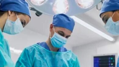 Three surgeons wearing blue scrubs and surgical masks, focused and ready for a surgical procedure in a sterile environment.