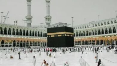 alt= Aerial view of the Kaaba surrounded by people walking in prayer at the Masjid al-Haram in Mecca.