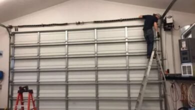 A man repairs a garage door inside a garage, focused on his task with tools nearby.