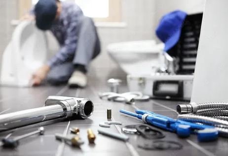 A man repairs a toilet using various plumbing tools, focused on his task in a well-lit bathroom setting.