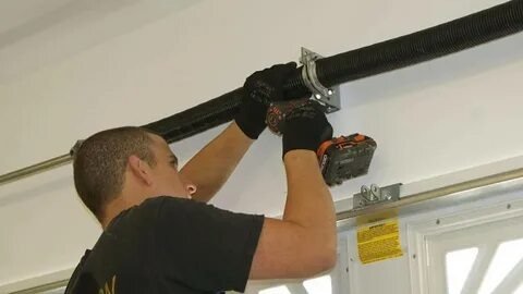 A man repairs a garage door using a tool, demonstrating hands-on maintenance and home improvement skills.