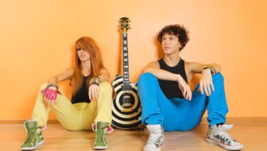 Two stylish women sitting with a guitar in the center, showcasing fashion influence in music.